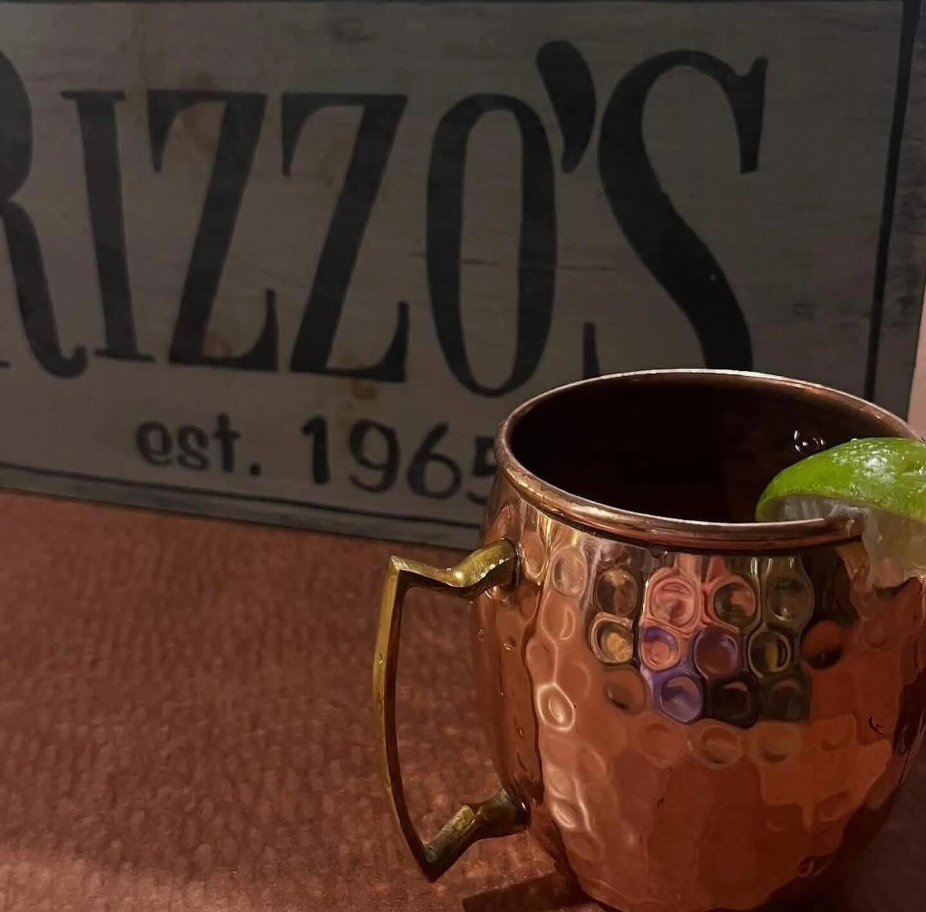 Copper mug cocktail in front of Rizzo's sign